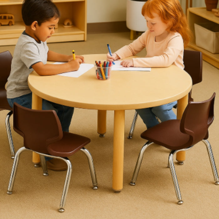 Two children sitting at a round table in a classroom setting, drawing with pencils.