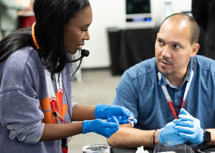Two people wearing blue gloves interacting with a small object in an indoor setting.