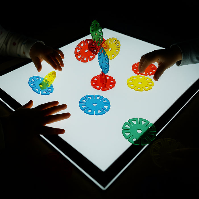 Children playing with colorful geometric shapes on a light-up board.