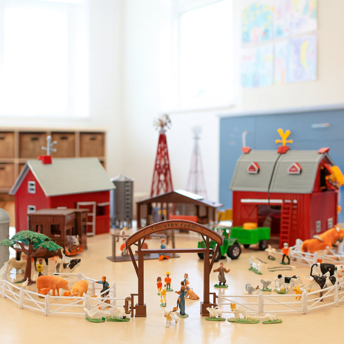 Model farm set with barns, animals, and people on a wooden floor.