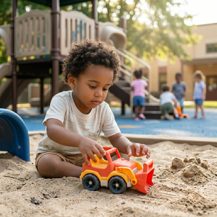 Child playing with a toy truck in a sandbox at a playground.