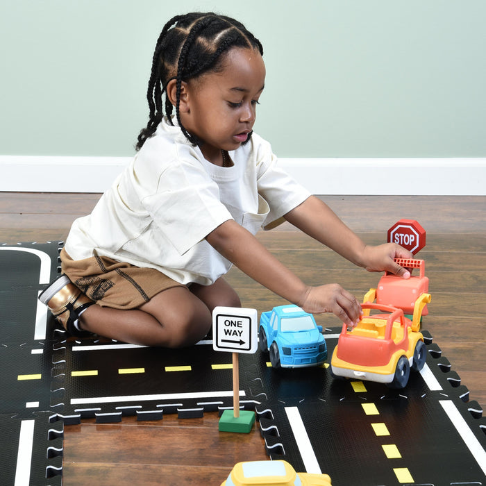 Child playing with toy cars and a stop sign on a road mat.