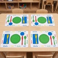 Four colorful children's table placemats arranged on a light wood table in a classroom setting. Each placemat shows labeled sections for knife, spoon, fork, plate, cup, and plate/cup with bright green, blue, red, yellow, and white colors.