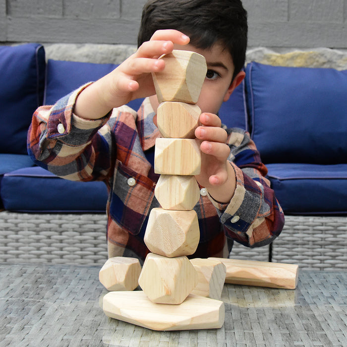 Child dressed in plaid shirt building with wooden balancing blocks with blue couch behind him
