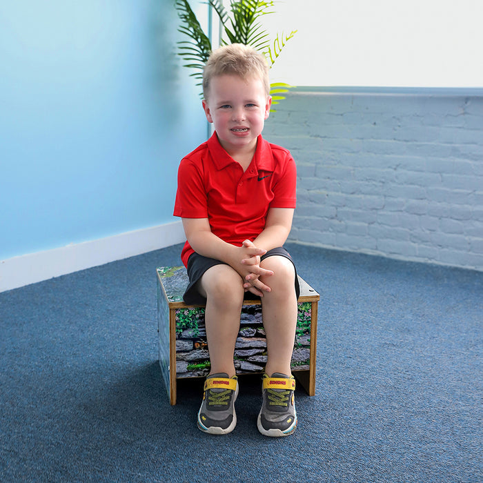 Young boy in a red shirt sitting on a small bench with a blue floor and white wall in the background