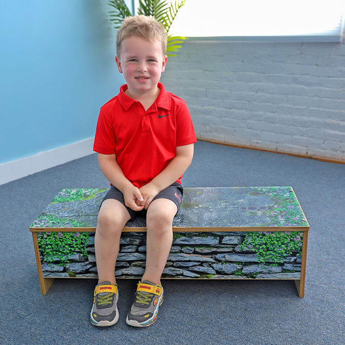 Child sitting on a bench with a stone and grass pattern in an indoor setting.