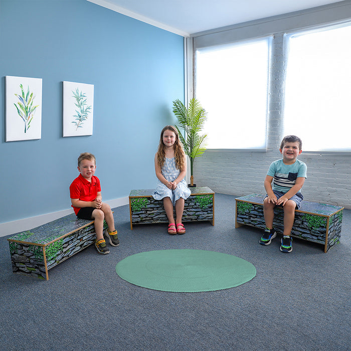 Three children sitting on stone benches in a room with blue walls and large windows.