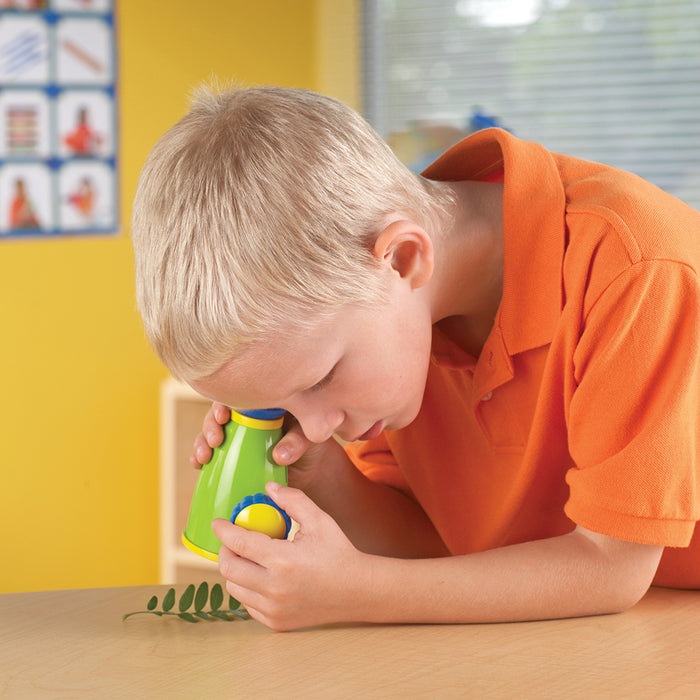 Child playing with a green toy magnifying glass in a classroom setting