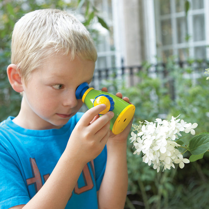 Child holding a toy telescope up to their eye, looking at flowers outdoors.