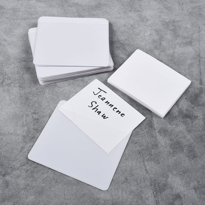 A stack of white adhesive labeling pockets on a grey surface, with one pocket displaying a written label.