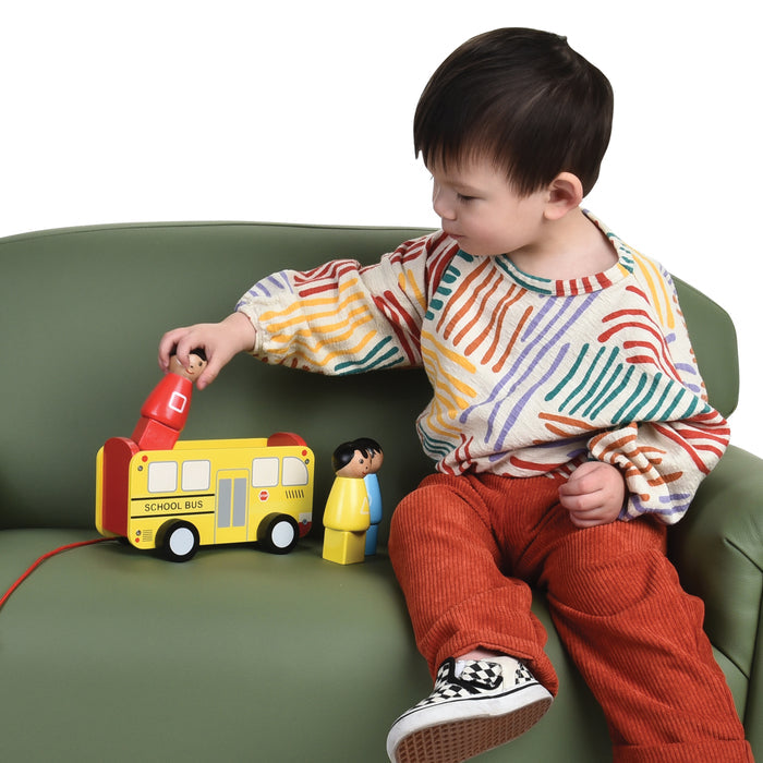 Child playing with a toy school bus on a green couch