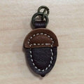 A brown leather zipper pull in the shape of an acorn with a metal ring on top.