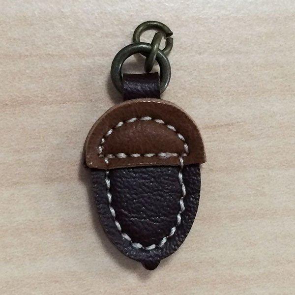 A brown leather zipper pull in the shape of an acorn with a metal ring on top.